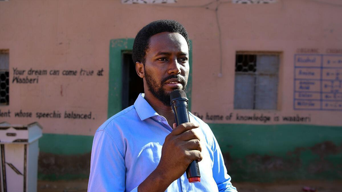 Mohamed Sheikh Said Haji speaks with a microphone in front of a school
