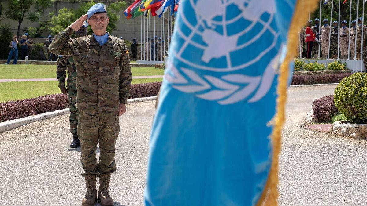 A peacekeeper salutes behind a UN flag.