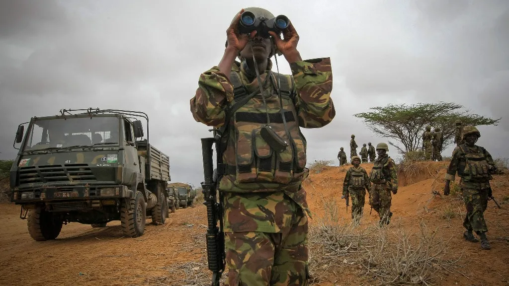 A military officer looks through binoculars with a tank in the background